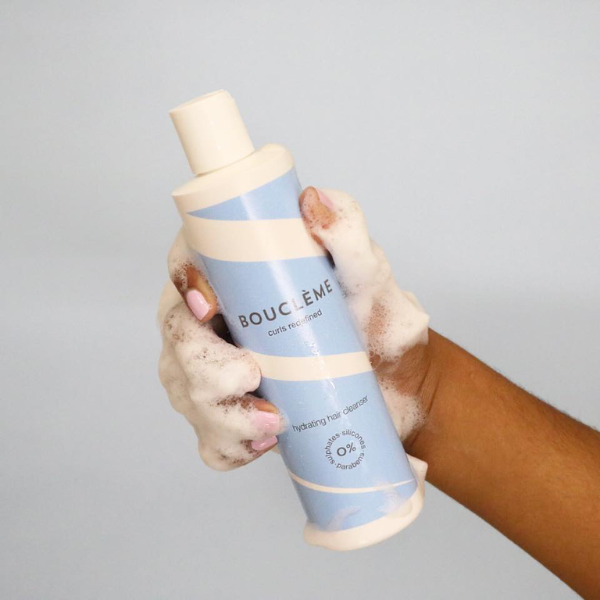 Iemand die de Boucleme Shampoo in haar hand heeft met schuim.