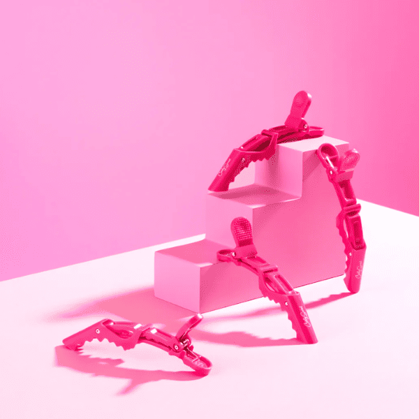 Vier roze Curly Secret alligator hair clips die speels zijn uitgestald op een roze achtergrond met een trapvormige standaard.