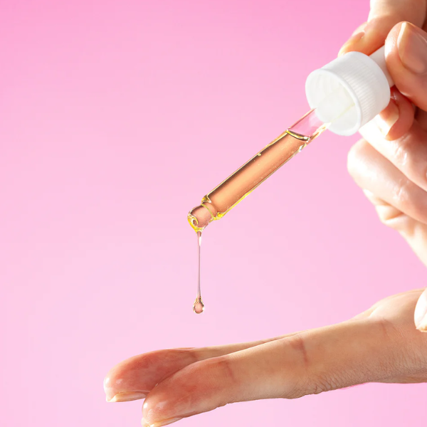 Close-up van een pipet waarmee Curly Secret Scrunching Oil wordt aangebracht, een druppel olie valt op de vingertoppen.