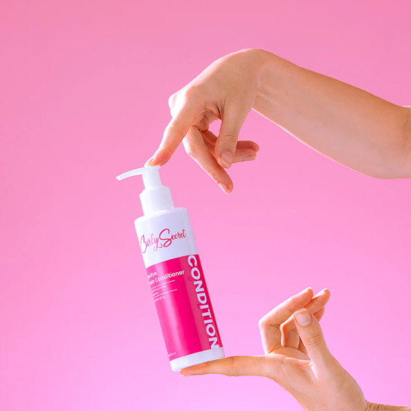Fles Curly Secret Bye Bye Knots Conditioner, vastgehouden door twee handen