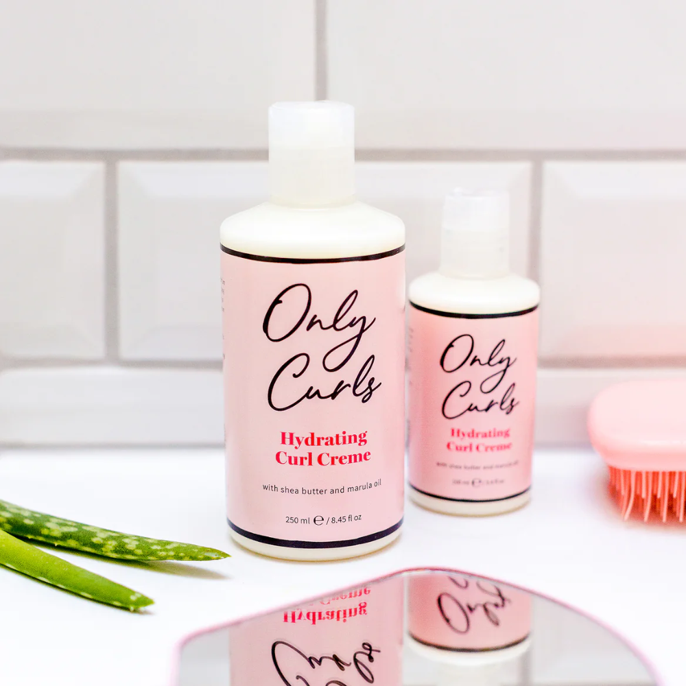 Only Curls Hydrating Curl Creme naast een kleinere fles en een roze borstel op een badkamertegel