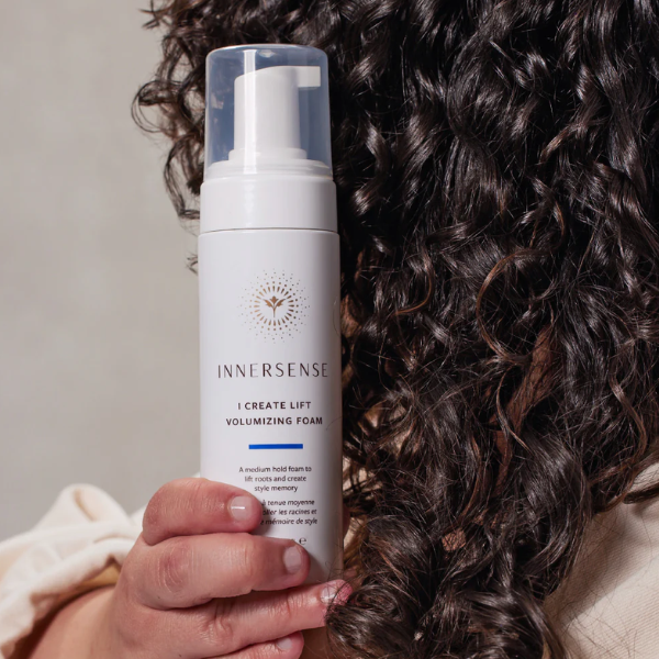 Iemand houd Innersense I Create Lift Volumizing Foam vast voor haar krullen