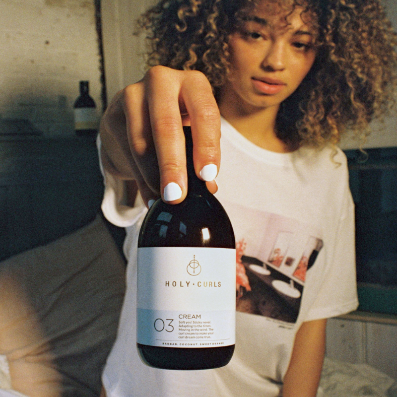 Vrouw met krullen die de Holy Curls Cream vast heeft